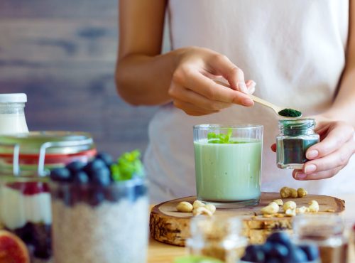 Female hands are preparing organic yogurt with spirulina for good digestion and functioning of gastrointestinal tract. Summer berries, nuts, fruits, dairy products on table. Healthy food concept.